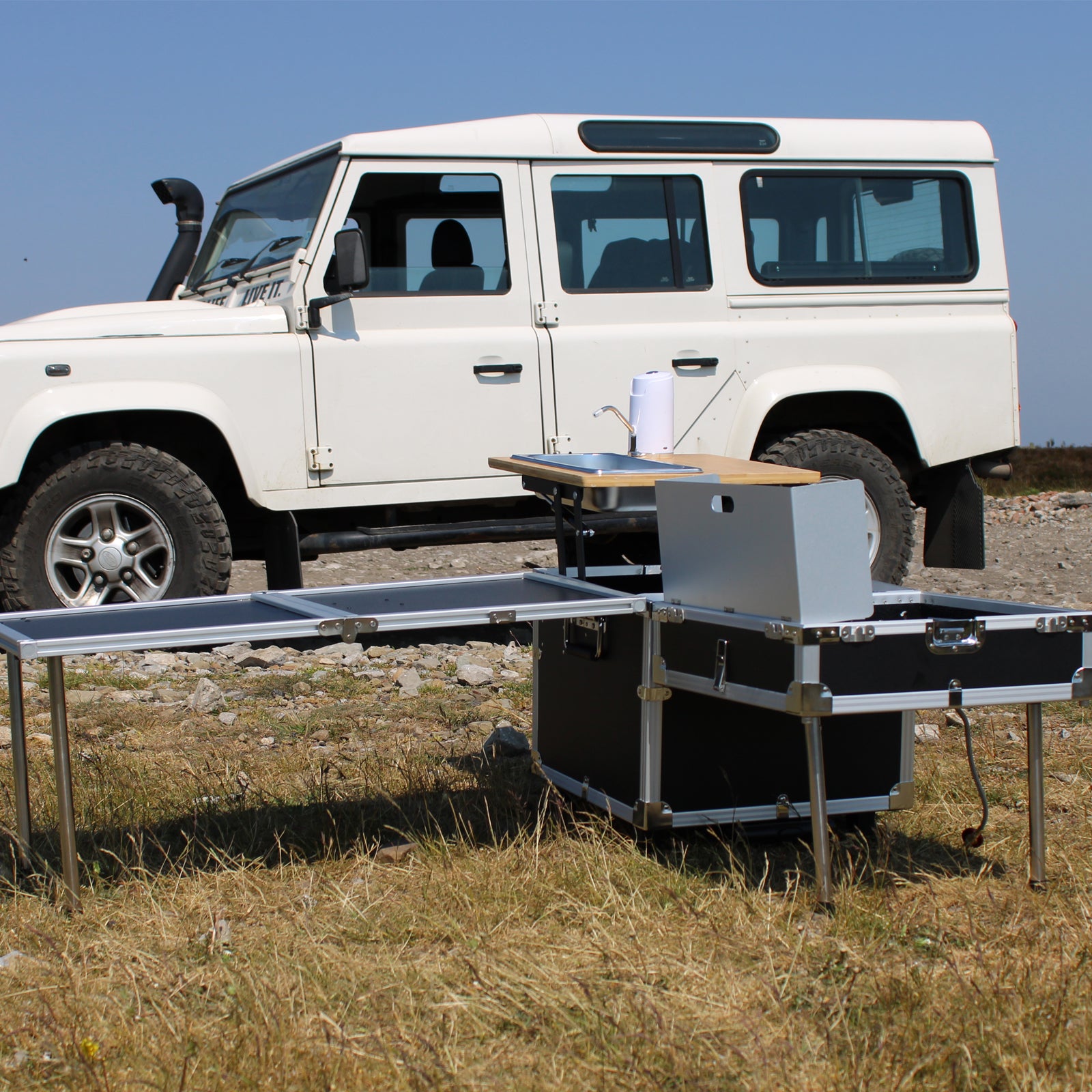 Compact portable kitchen with a Land Rover in the background.